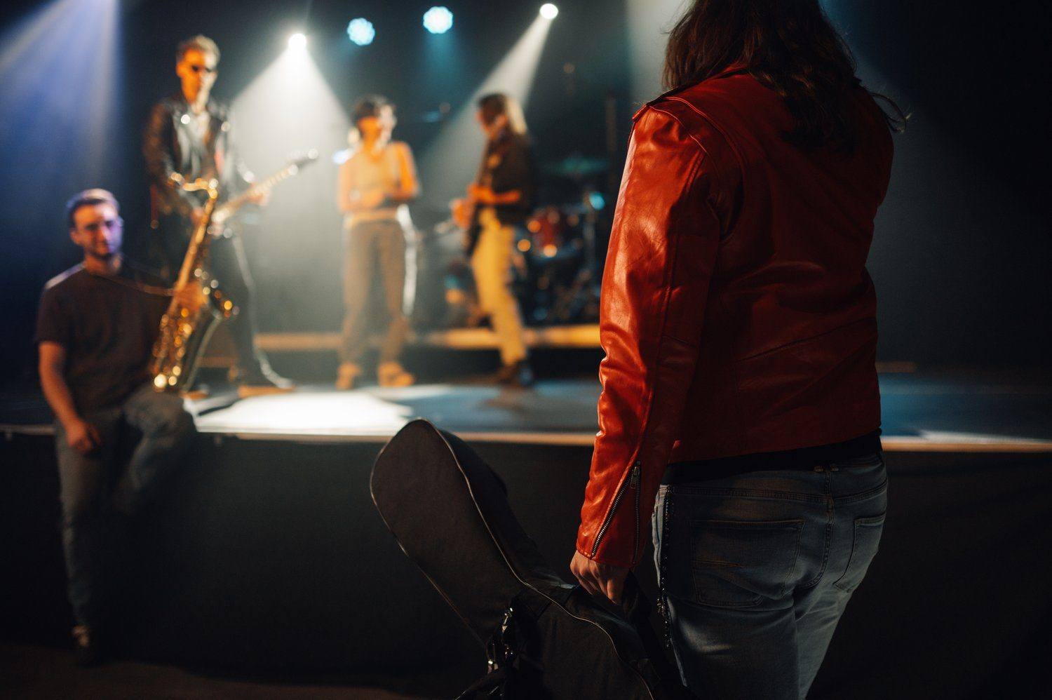 Zespół na małej scenie klubowej w ciepłym świetle, publiczność widziana od tyłu